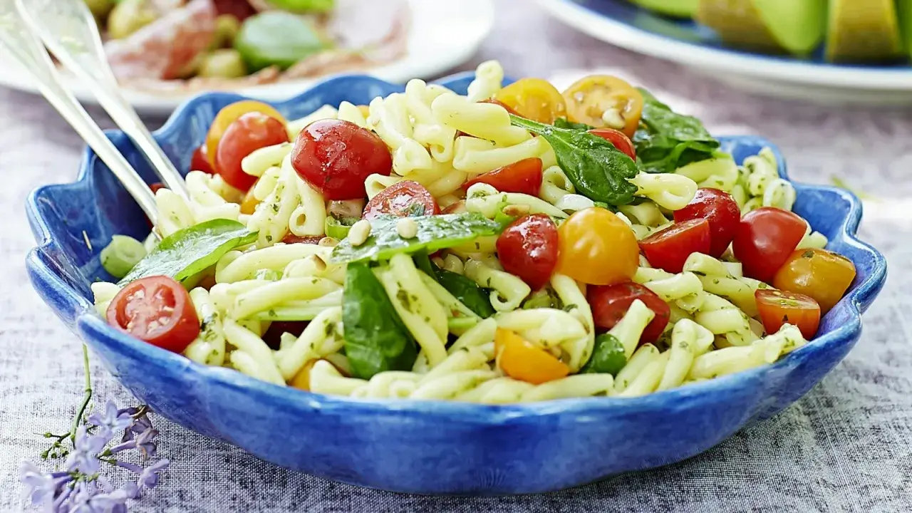 En härlig italiensk pastasallad med körsbärstomater och basilika i en blå skål, perfekt för en sommarlunch.