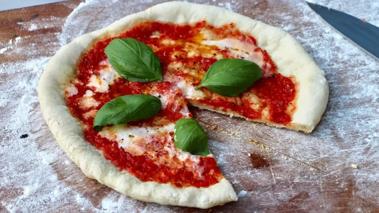 En nybakad pizza på grillen, med tomatsås, mozzarella och färsk basilika, redo att avnjutas.