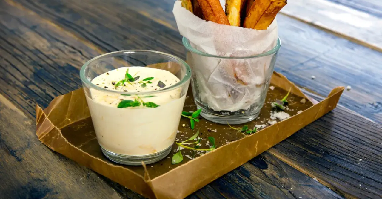 En krämig creme fraiche sås med örter, serverad bredvid en glasburk med pommes frites på ett rustikt träbord.