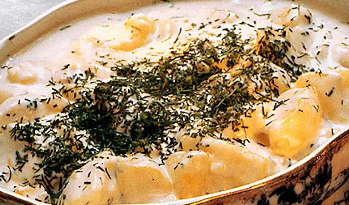 En krämig stuvad potatis med dill, serverad i ett vackert uppläggningsfat.