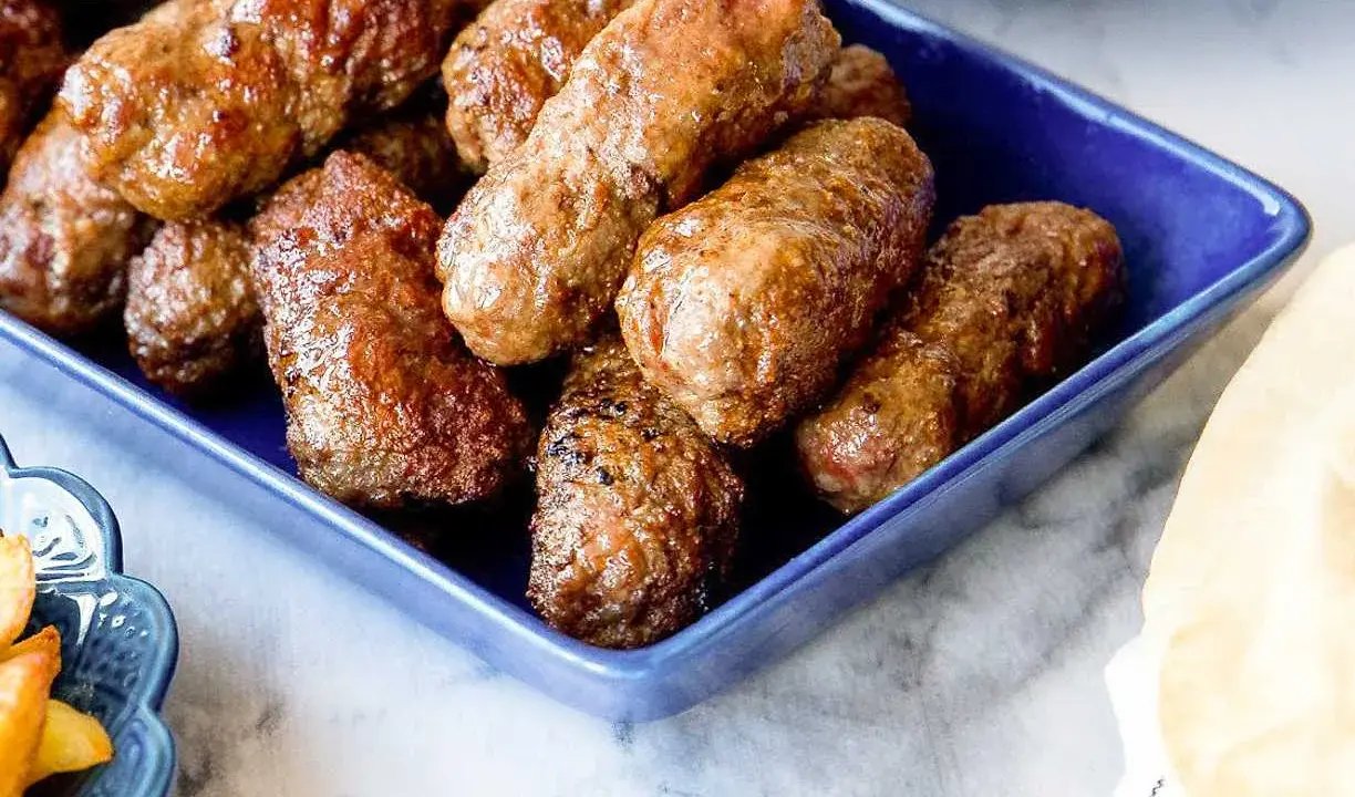 En blå skål fylld med saftiga cevapcici, redo att avnjutas. Ett perfekt cevapcici recept för alla köttälskare.
