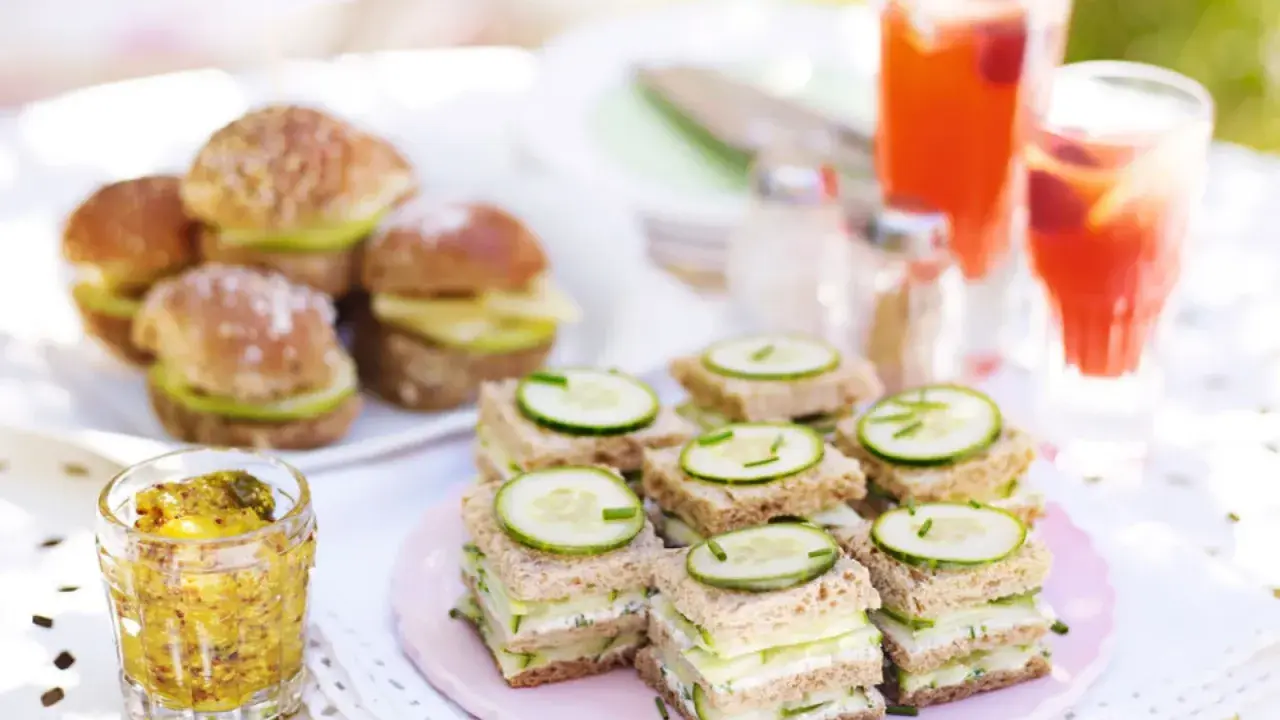 Små smörgåsar med gurka och ost, perfekta för ett afternoon tea recept. Serveras med röda drycker och senap.