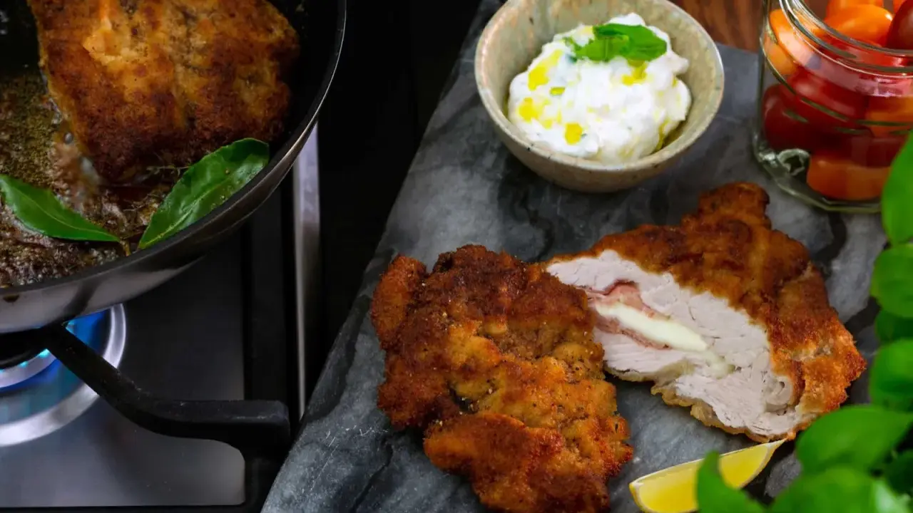 Krispig schnitzel med ost och skinka, serverad med en krämig sås till schnitzel, citron och körsbärstomater.