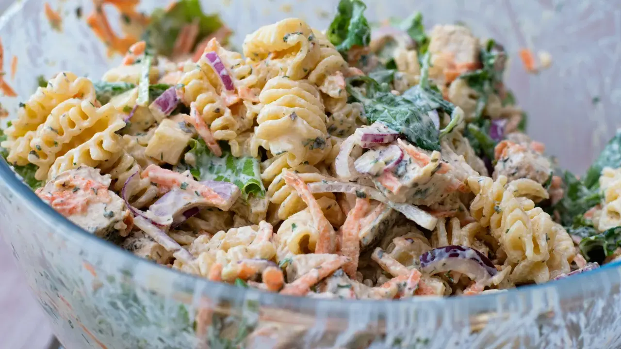 En stor skål med krämig pastasallad med kyckling, morötter, rödlök och gröna blad. Perfekt för en somrig picknick.