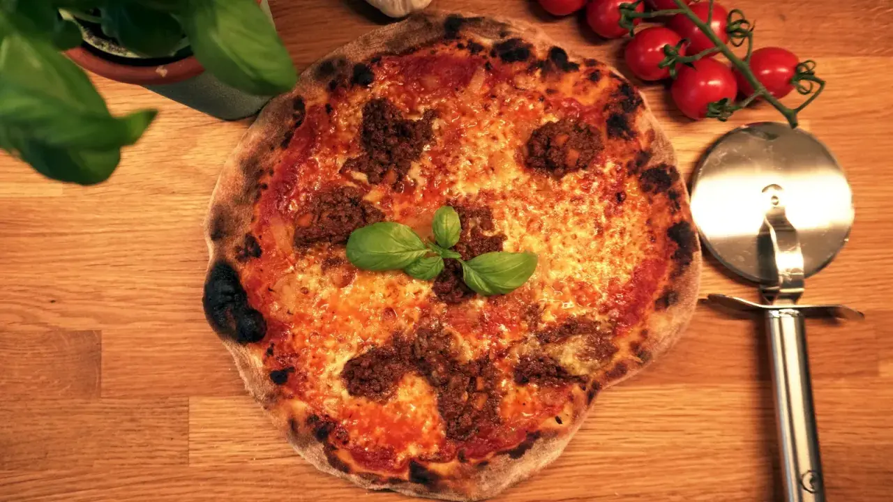 En härlig napolitansk pizza med köttfärs och basilika, redo att skäras med pizzaskäraren.