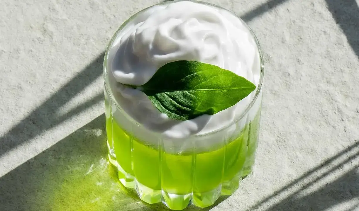 En uppfriskande grön drink med fluffigt kokosskum och ett grönt blad som dekoration. Perfekt för en solig dag.