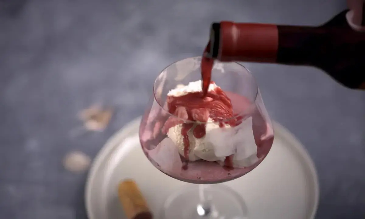 En flaska häller upp rött dessertvin till glass i ett glas. En perfekt kombination för en lyxig efterrätt.