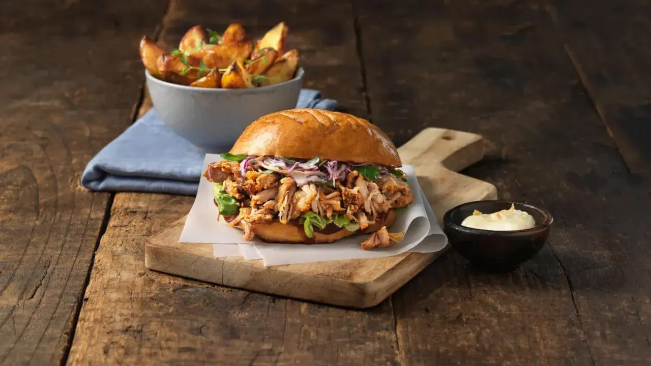 En saftig pulled pork burgare med krispig kål och en skål med ugnsrostade potatisklyftor.
