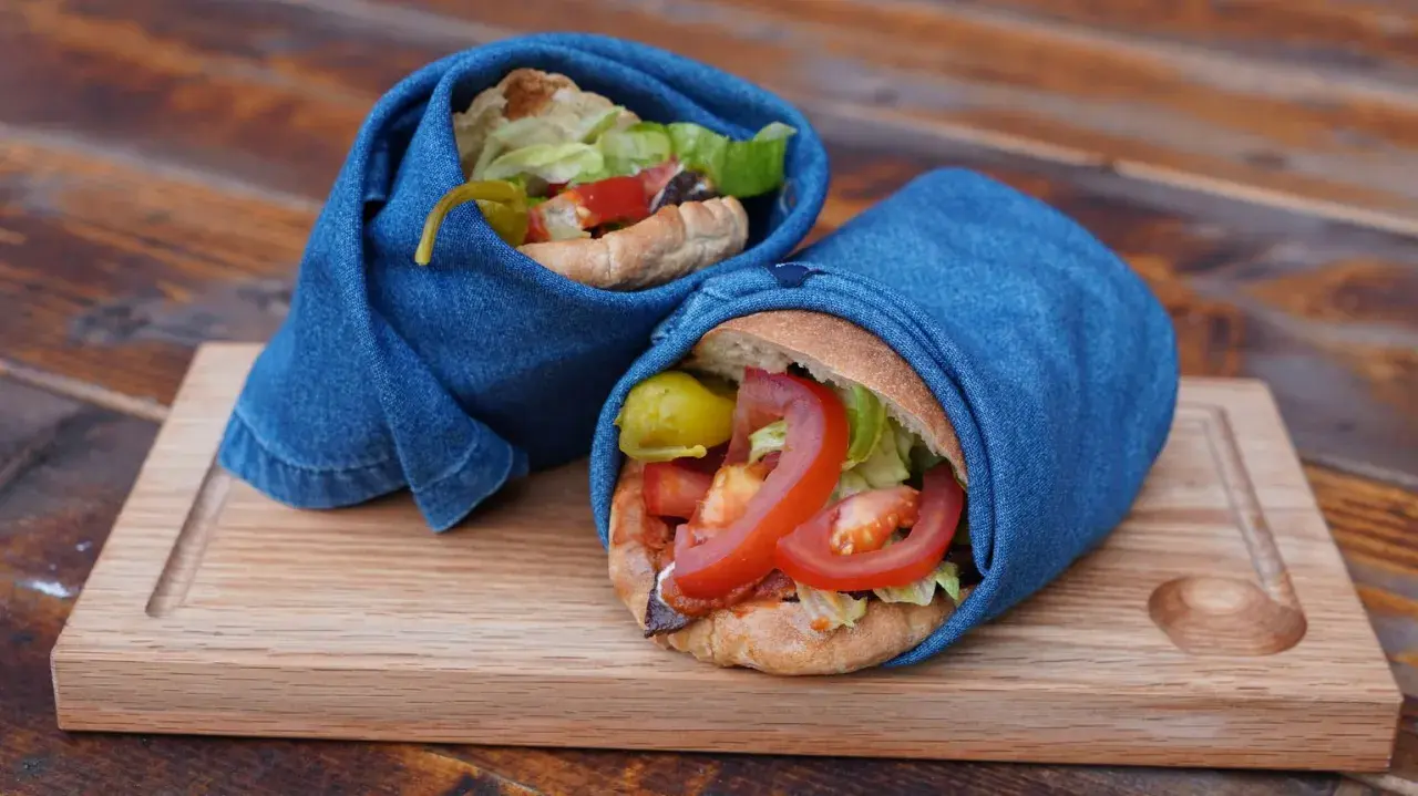 Två kebabrullar inslagna i jeans på en träbricka. Ett enkelt kebab recept med färska grönsaker.