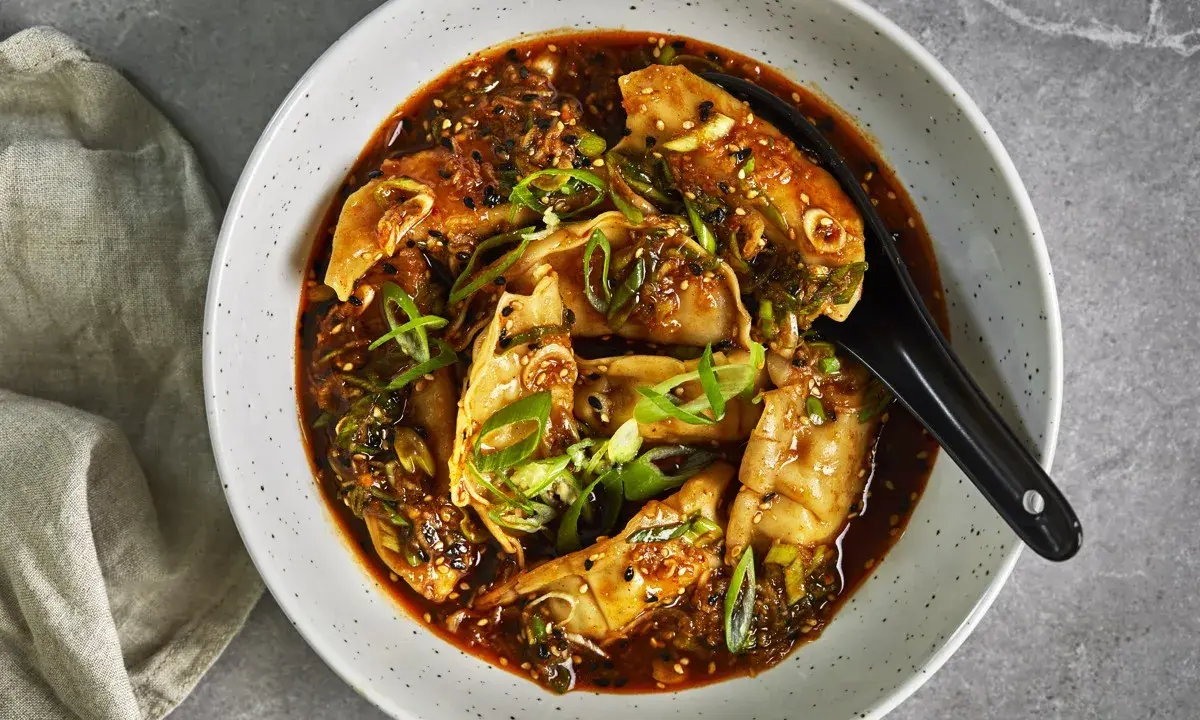 En skål med dumplings i en kryddig sås, toppad med salladslök och sesamfrön. Ett perfekt lunch recept för en smakrik måltid.