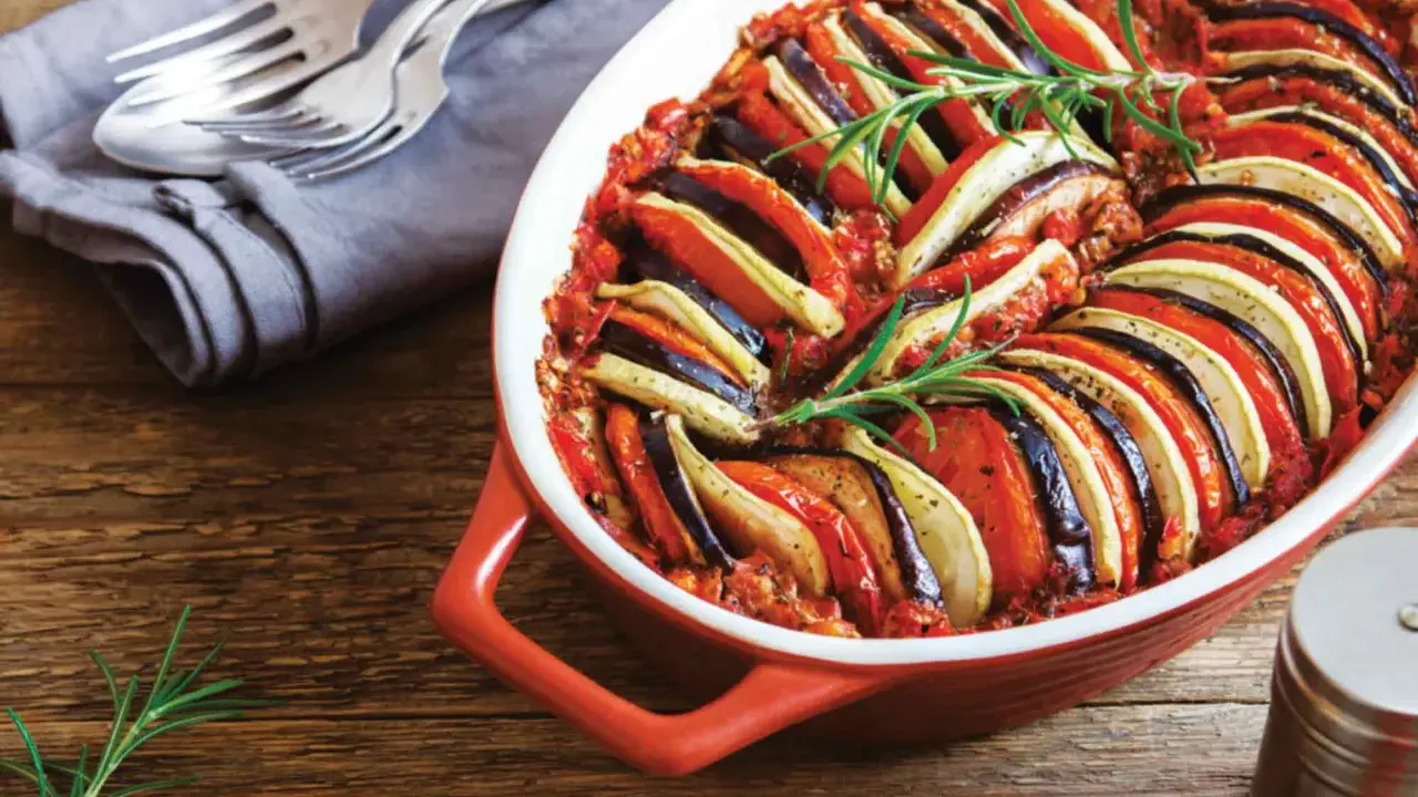 En vackert upplagd ratatouille i en ugnsform, perfekt för en nyttig middag. Grönsakerna är skivade och arrangerade i ett mönster, toppad med rosmarin.