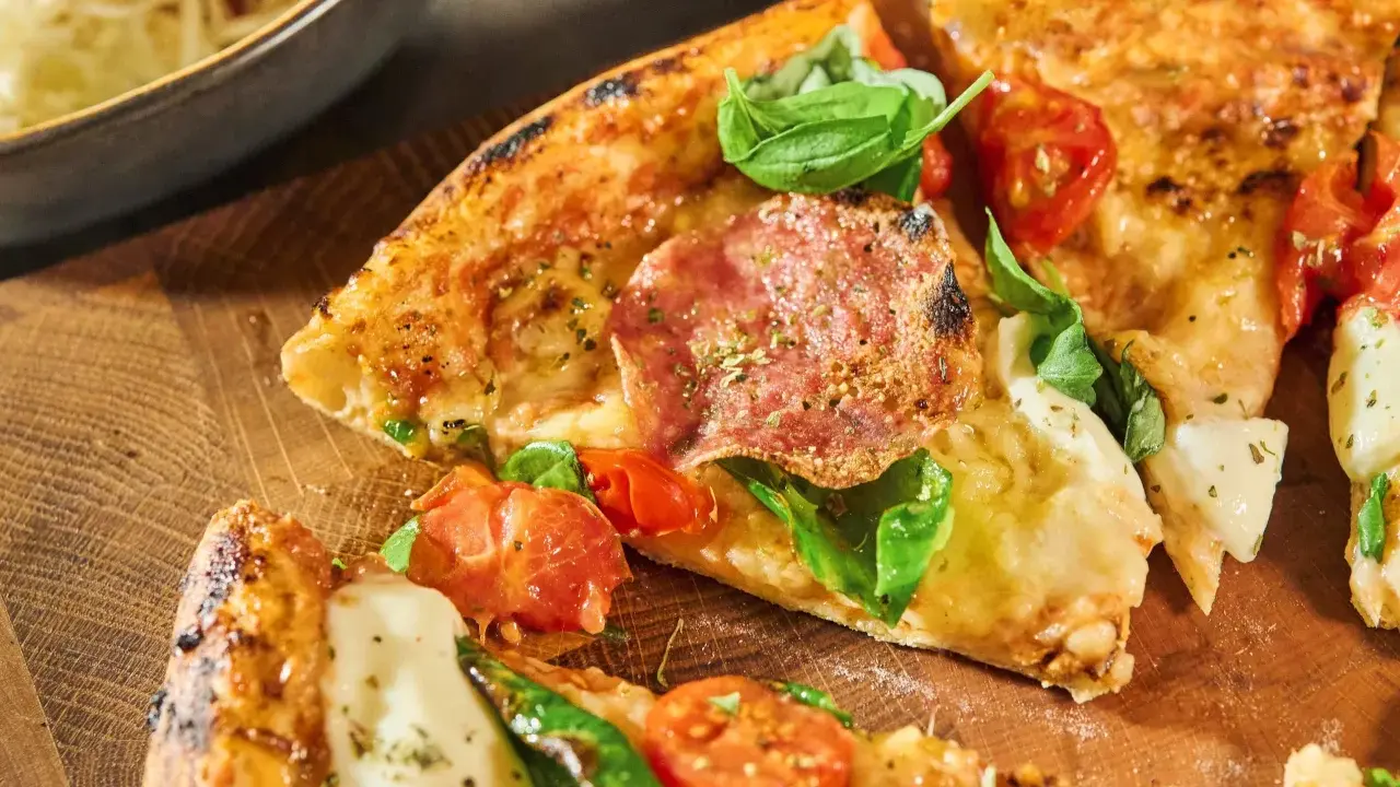 Fredriks fika: Krispig pizzadeg med salami, tomater och färsk basilika på en träskärbräda.