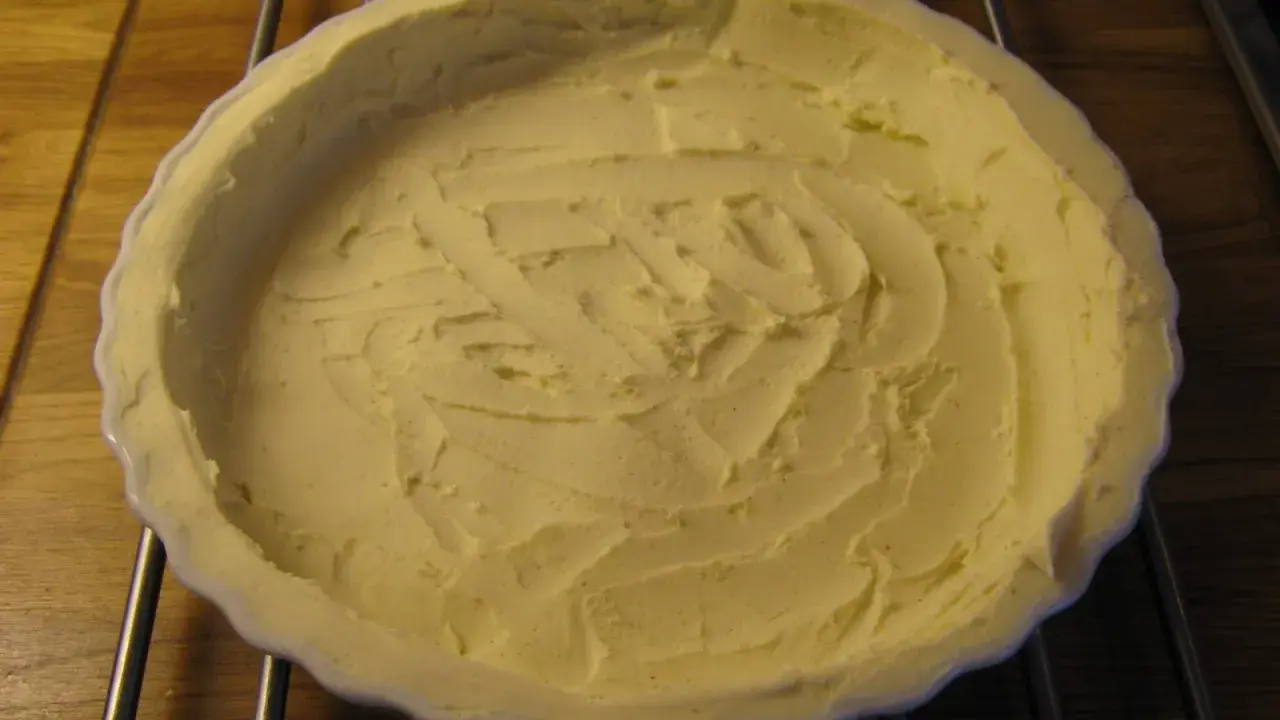 En vit pajform med en färdig glutenfri pajdeg från Lailas. Pajdegen är pressad mot formens kanter och har ett mönster i mitten.