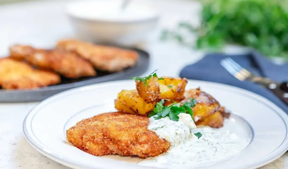 En tallrik med krispig panerad kyckling, rostade potatisklyftor och en krämig dillsås. En klassisk svensk rätt som ser utsökt ut.