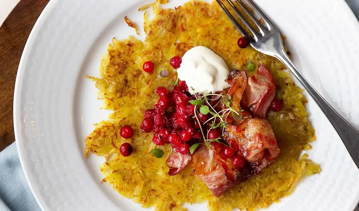 En gyllene råraka med knaperstekt bacon, lingon och en klick gräddfil. Ett klassiskt råraka recept som är perfekt för en helgmåltid.