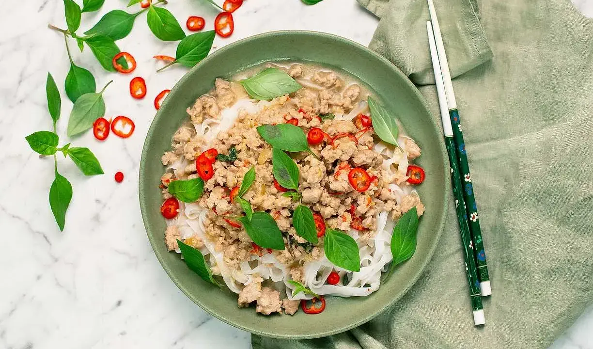 En skål med nudlar och köttfärs, toppad med färsk basilika och chili. En härlig thai mat som ser utsökt ut.