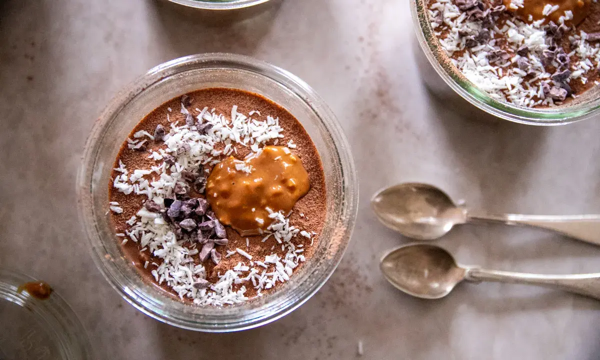 Chokladpudding med kokosflingor och kakaonibs, en perfekt proteinrik frukost. Två skedar ligger bredvid.