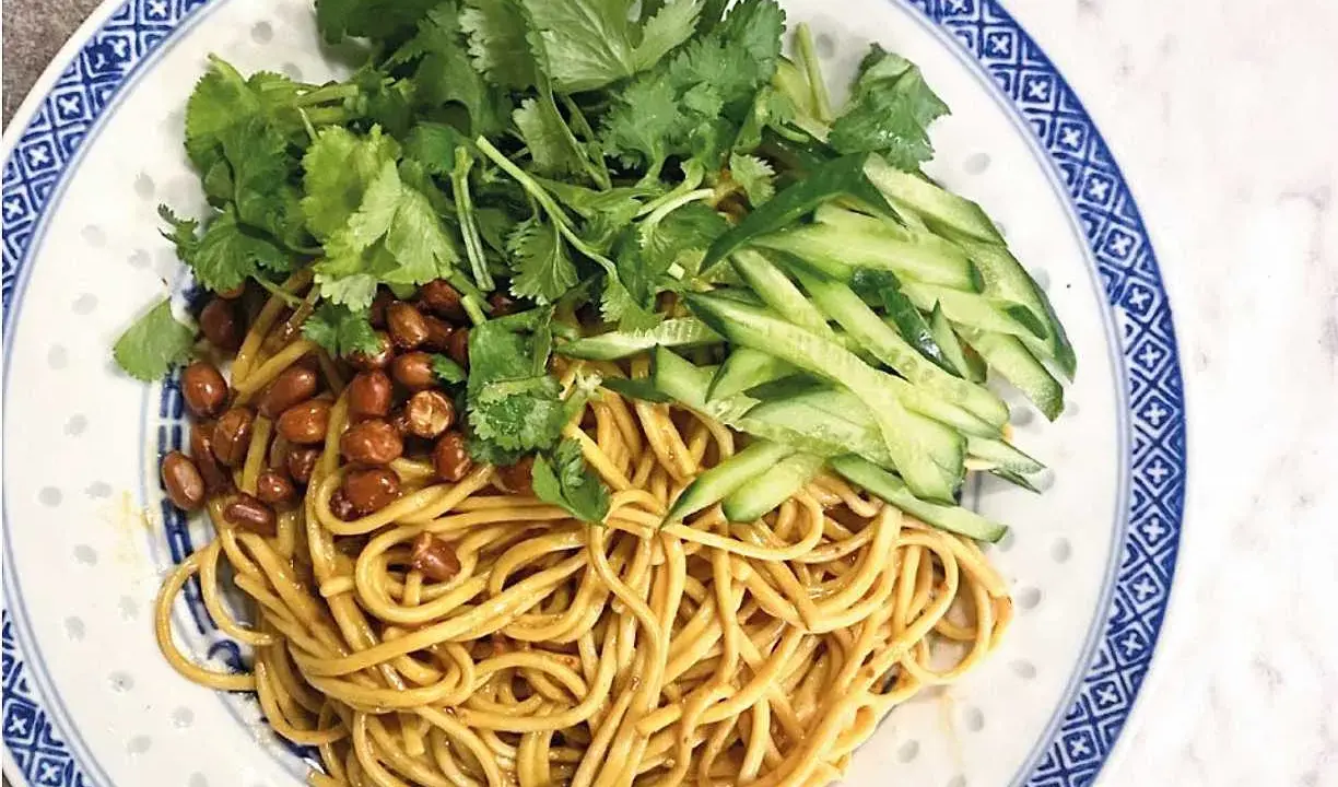En läcker asiatisk nudelsallad med krispig gurka, rostade jordnötter och färsk koriander på en vackert mönstrad tallrik.