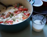 En krämig kreolsk gryta med korv, paprika, oliver och pickles i en blå gryta. En skål med mjölk står bredvid.