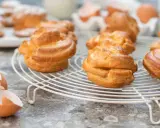 Nybakade petit choux på ett vitt galler, med äggskal och ägg i bakgrunden. Perfekt för fyllning!