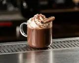 En mugg med vispad grädde, kanel och chokladpulver. Denna godaste varm choklad ser inbjudande ut.