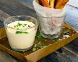 En krämig creme fraiche sås med örter, serverad bredvid en glasburk med pommes frites på ett rustikt träbord.