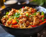 En läcker kyckling wok med nudlar, grönsaker och sesamfrön i en svart skål.