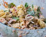 En stor skål med krämig pastasallad med kyckling, morötter, rödlök och gröna blad. Perfekt för en somrig picknick.