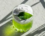 En uppfriskande grön drink med fluffigt kokosskum och ett grönt blad som dekoration. Perfekt för en solig dag.