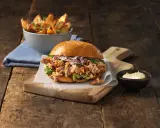En saftig pulled pork burgare med krispig kål och en skål med ugnsrostade potatisklyftor.