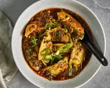 En skål med dumplings i en kryddig sås, toppad med salladslök och sesamfrön. Ett perfekt lunch recept för en smakrik måltid.