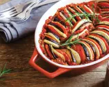 En vackert upplagd ratatouille i en ugnsform, perfekt för en nyttig middag. Grönsakerna är skivade och arrangerade i ett mönster, toppad med rosmarin.