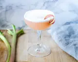 En rosa drink med rabarbersirap och gin, garnerad med en rabarberskiva. Bredvid syns färska rabarberstjälkar.
