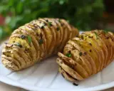 Två gyllene hasselbackspotatisar med örter, redo att serveras. Ett perfekt hasselbackspotatis recept för middagen.