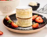 Två fluffiga japanska pannkakor staplade på en svart tallrik, garnerade med florsocker och färska jordgubbar.