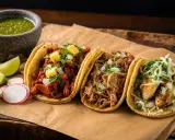 Tre läckra tacos med olika fyllningar, en skål med grön sås och limeklyftor. En härlig måltid med mexikansk mat.