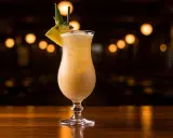 En krämig virgin piña colada, dekorerad med ananas och ett sugrör, står på en träbar med bokeh-ljus i bakgrunden.