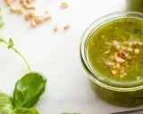 Färska basilikablad och pinjenötter bredvid en burk med hemlagad pesto genovese recept.