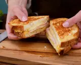 En gyllene croque monsieur, perfekt rostad och fylld med ost och skinka, delas på ett skärbräde.