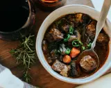 En skål med mustig boeuf bourguignon, perfekt för ett mysigt recept. Serveras med en sked och en kvist rosmarin.