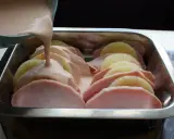 Kassler med ananas förbereds i en ugnsform. En krämig sås hälls över skivorna av kassler och ananas.