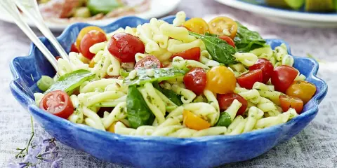 En härlig italiensk pastasallad med körsbärstomater och basilika i en blå skål, perfekt för en sommarlunch.