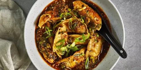 En skål med dumplings i en kryddig sås, toppad med salladslök och sesamfrön. Ett perfekt lunch recept för en smakrik måltid.