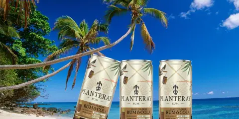Tre burkar rom och cola står på en tropisk strand med palmer och blå himmel.