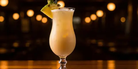En krämig virgin piña colada, dekorerad med ananas och ett sugrör, står på en träbar med bokeh-ljus i bakgrunden.