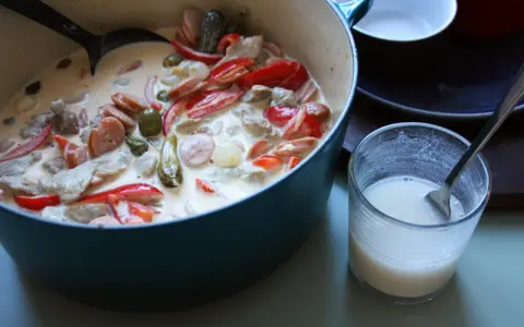 En krämig kreolsk gryta med korv, paprika, oliver och pickles i en blå gryta. En skål med mjölk står bredvid.