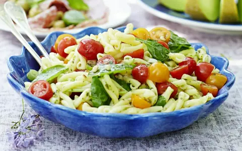 En härlig italiensk pastasallad med körsbärstomater och basilika i en blå skål, perfekt för en sommarlunch.