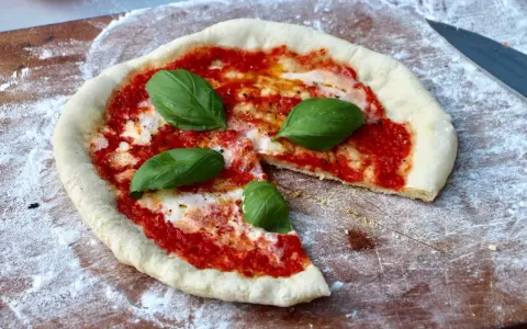 En nybakad pizza på grillen, med tomatsås, mozzarella och färsk basilika, redo att avnjutas.