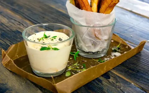 En krämig creme fraiche sås med örter, serverad bredvid en glasburk med pommes frites på ett rustikt träbord.