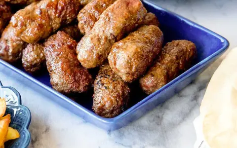 En blå skål fylld med saftiga cevapcici, redo att avnjutas. Ett perfekt cevapcici recept för alla köttälskare.
